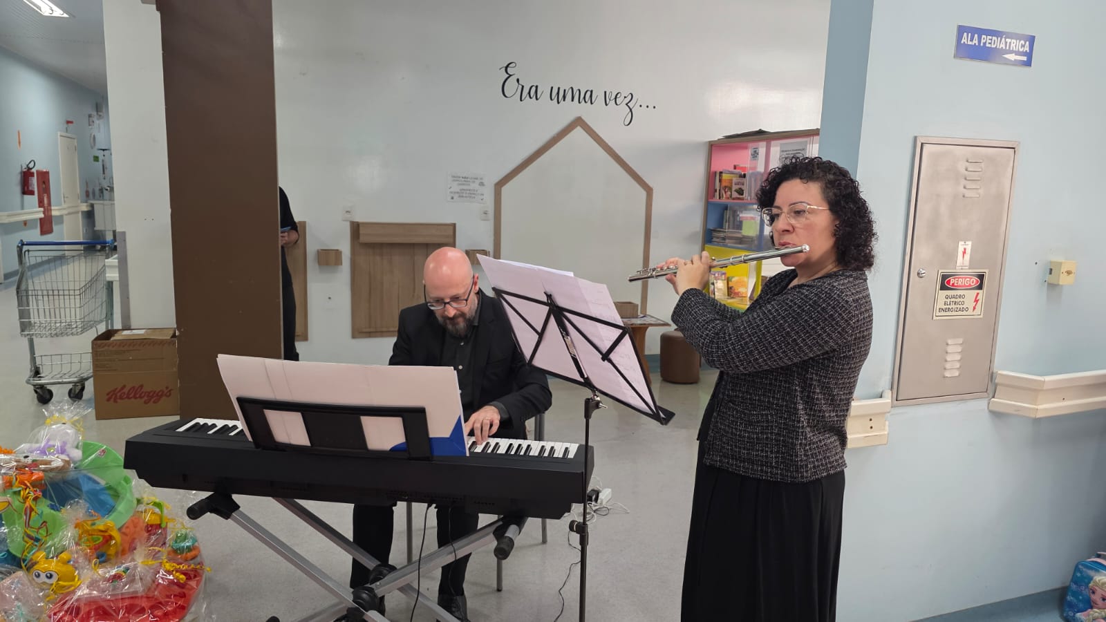 Músicos da Orquestra Sinfônica tocando teclado e flauta no corredor do Hospital da Criança