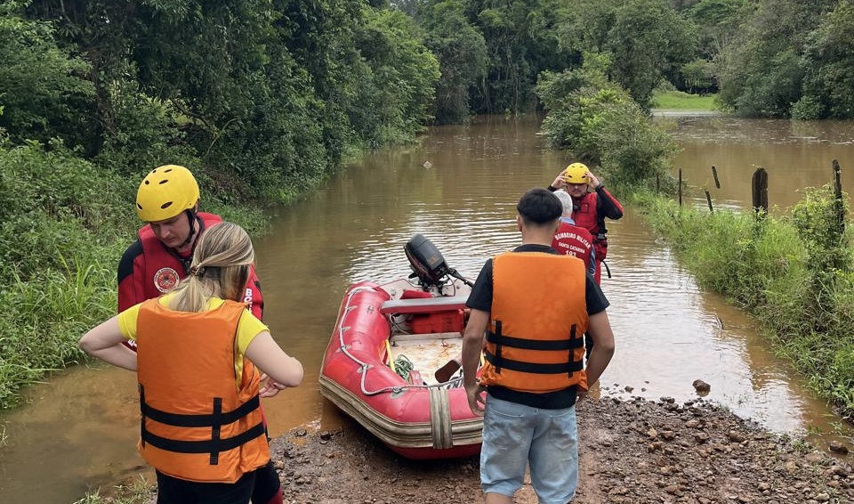 Bombeiros e moradores com colete salva-vidas ao lado de bote à beira de área alagada em Águas de Chapecó