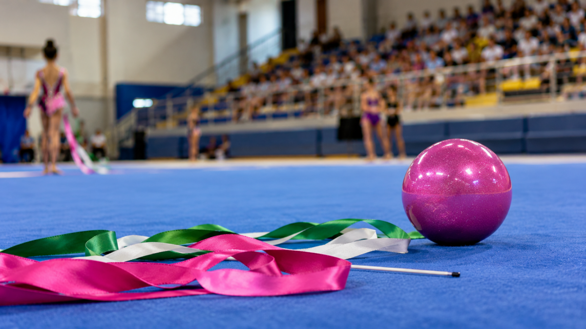 Bola rosa e fitas de ginástica rítmica sobre o tatame azul de um ginásio durante competição