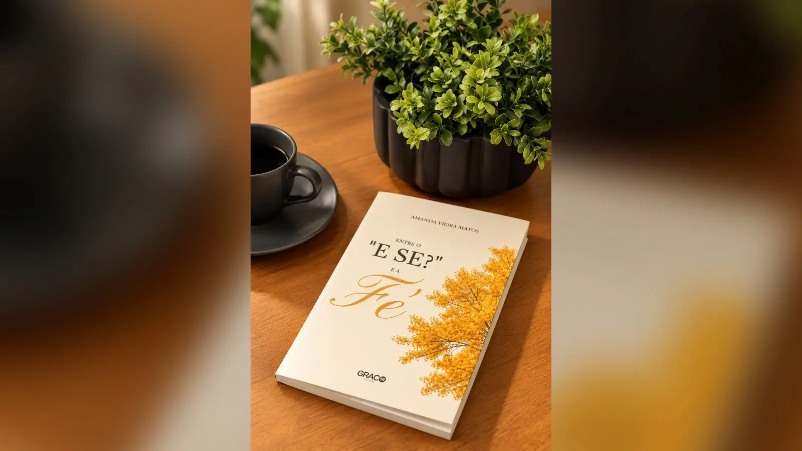 Livro “Entre o ‘e se?’ e a Fé”, de Amanda Vieira Matos, sobre uma mesa de madeira ao lado de uma xícara de café e de um vaso de planta